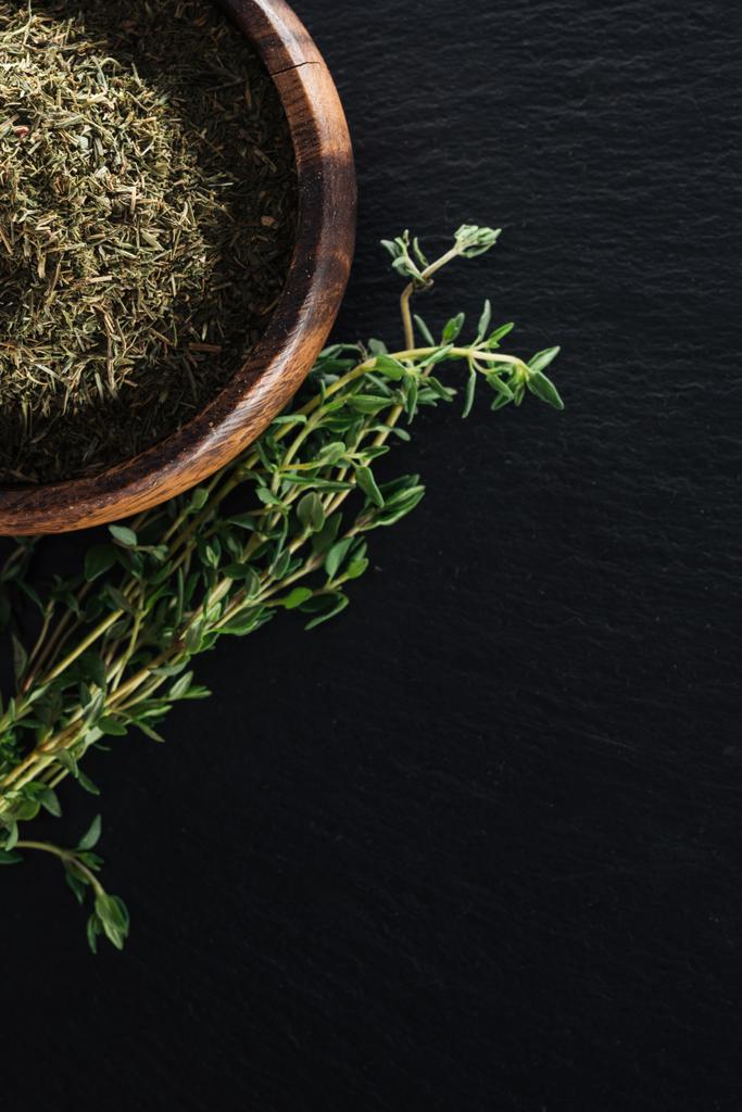 top view of dried thyme in wooden bowl near green herb on black background - Photo, Image