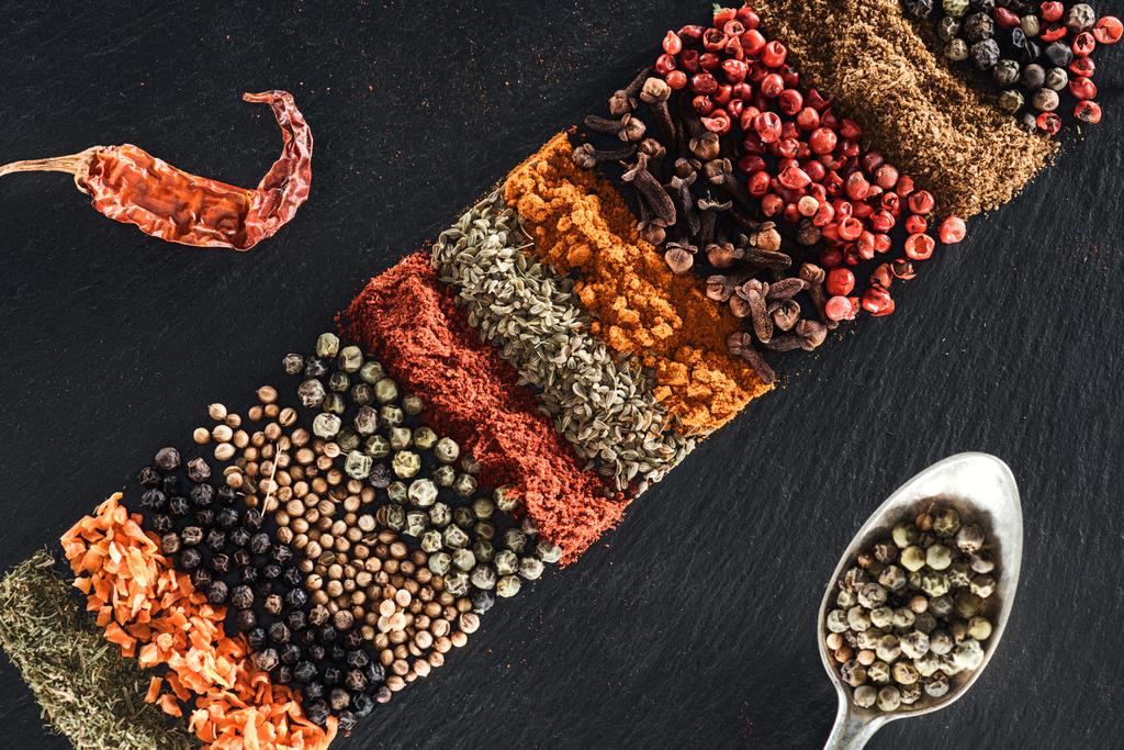top view of traditional indian spices on textured black background near spoon with white pepper and dried chili pepper - Photo, Image