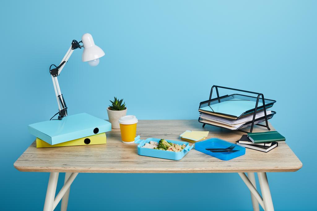 Studio shot van werkruimte met tafel en lunch box op blauwe achtergrond - Foto, afbeelding