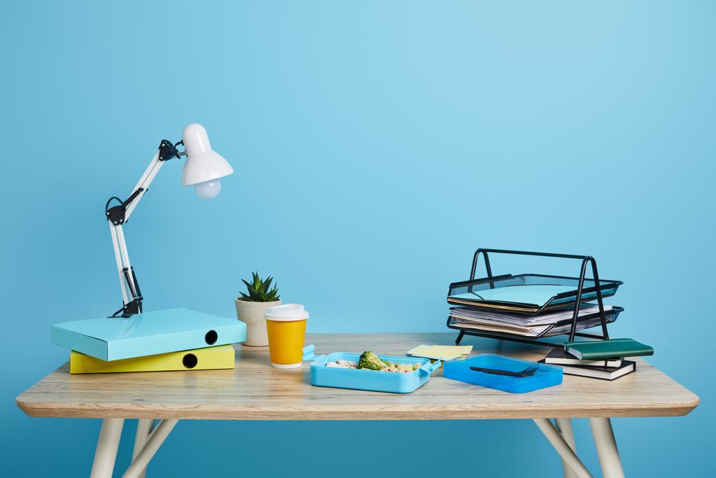 workspace with lunch box and coffee to go on wooden table on blue background - Foto, afbeelding