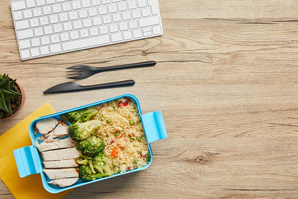 Ahşap masa üzerinde bilgisayar klavye yakınında pirinç, brokoli ve tavuk ile öğle yemeği kutusunun üst görünümü - Fotoğraf, Görsel