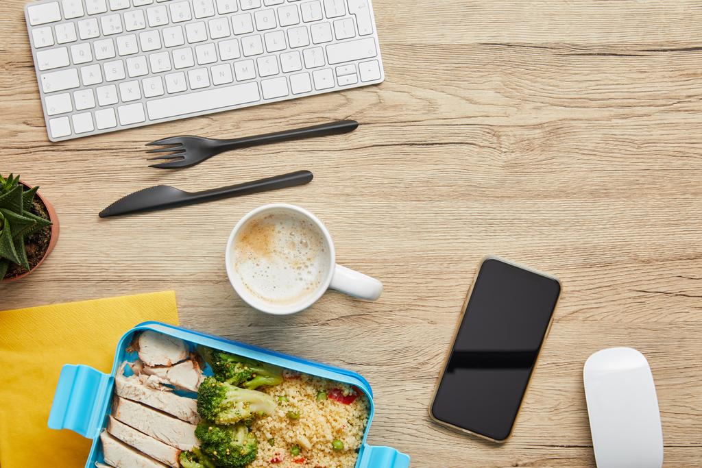 Вид на обеденную коробку с вкусной едой, горячими напитками и цифровыми приборами на деревянном столе
 - Фото, изображение