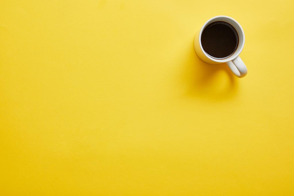 Κορυφαία θέα του φλιτζάνι ζεστό νόστιμο καφέ σε κίτρινο φόντο - Φωτογραφία, εικόνα