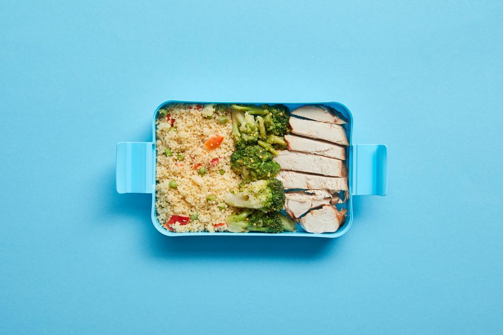 Κορυφαία θέα στο κουτί του μεσημεριανού γεύματος με νόστιμο κοτόπουλο, ριζότο και μπρόκολο σε μπλε φόντο - Φωτογραφία, εικόνα