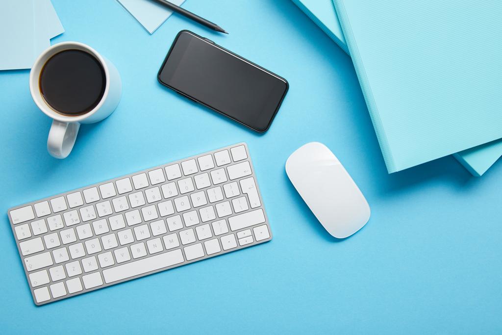 Κορυφαία προβολή του χώρου εργασίας με ψηφιακές συσκευές, χαρτιά και φλιτζάνι καφέ σε μπλε φόντο - Φωτογραφία, εικόνα