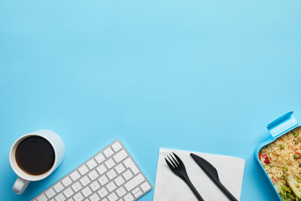 Вид зверху комп'ютерної клавіатури, чашка кави, обідня коробка зі смачною їжею та одноразова виделка з ножем на синьому фоні
 - Фото, зображення