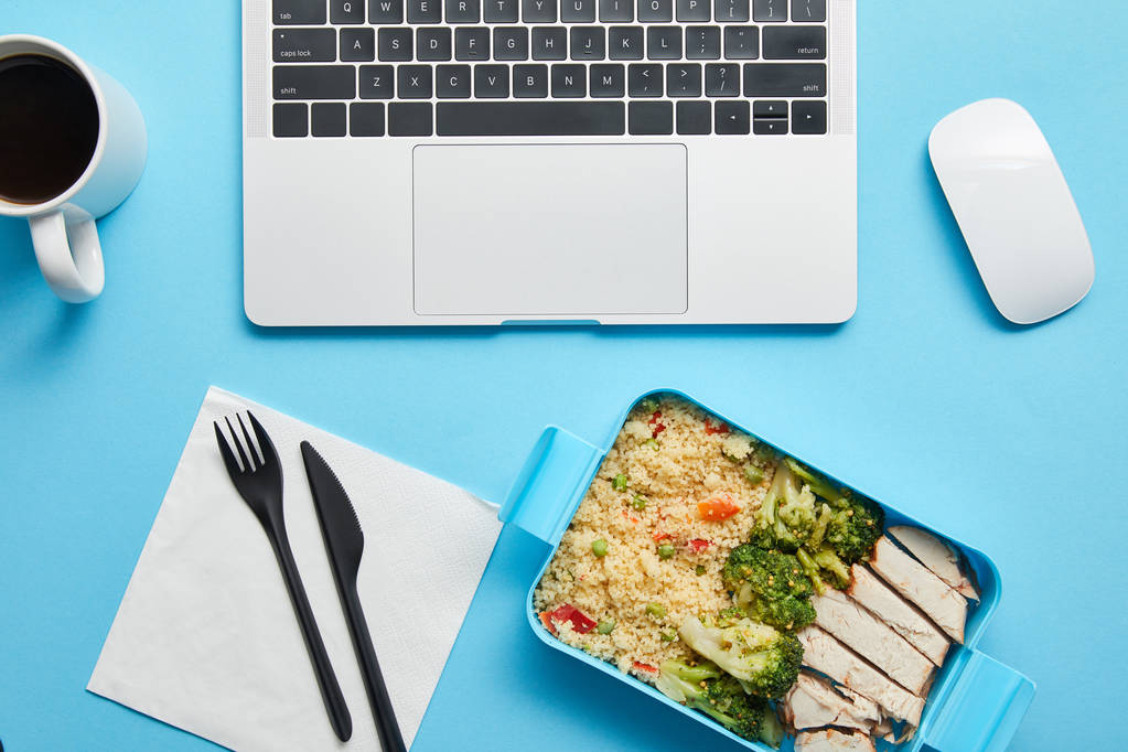 Widok z góry na urządzenia cyfrowe, filiżankę kawy i lunch box ze smacznym kurczakiem, ryżem i brokułami na niebieskim tle, ilustrujący redakcyjny - Zdjęcie, obraz