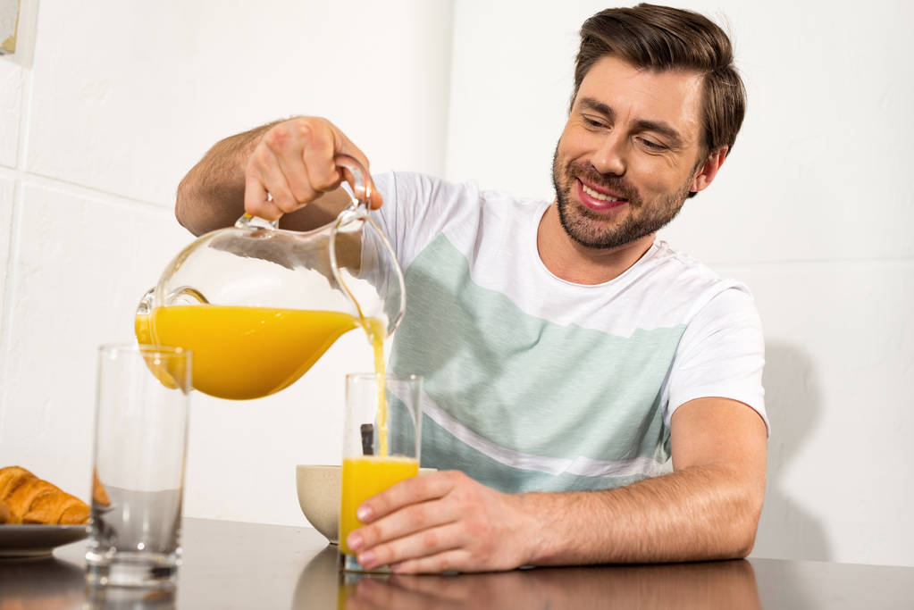 homme souriant verser du jus d'orange dans le verre pendant le petit déjeuner dans la cuisine
 - Photo, image