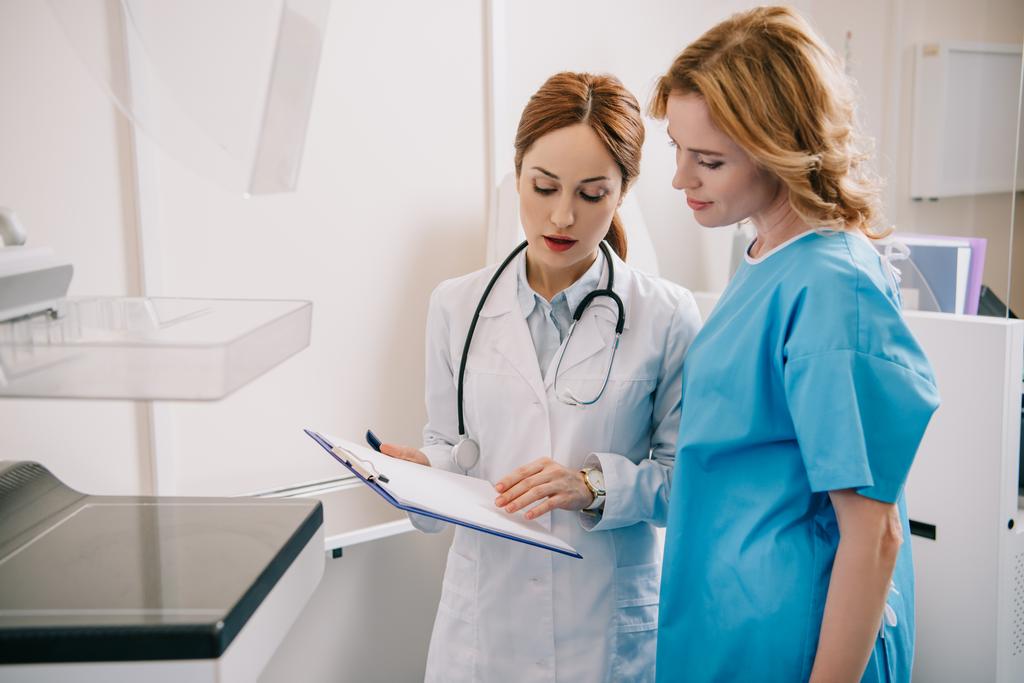 aantrekkelijke jonge arts en patiënt kijken naar de diagnose op het Klembord - Foto, afbeelding