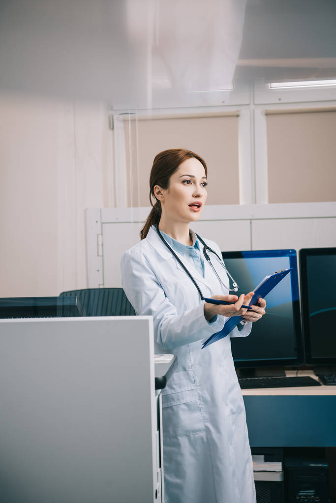 selective focus of pretty young doctor gesturing while holding clipboard  - Photo, Image