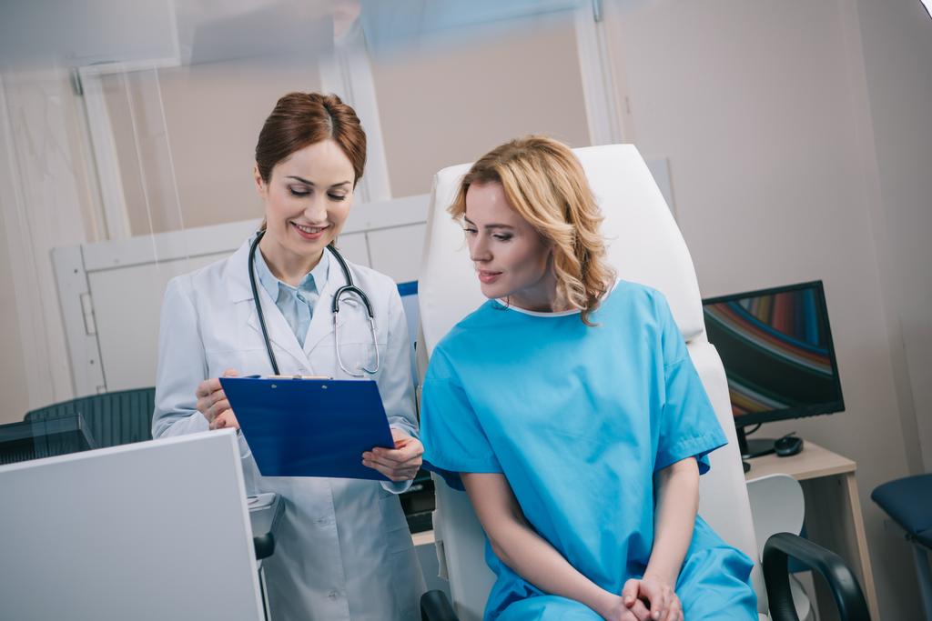 pretty young doctor and smiling patient looking at clipboard with diagnosis - Photo, Image