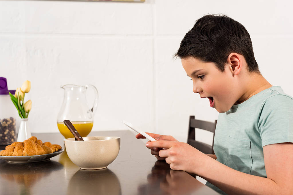 scioccato ragazzo utilizzando tablet digitale durante la colazione in cucina
 - Foto, immagini