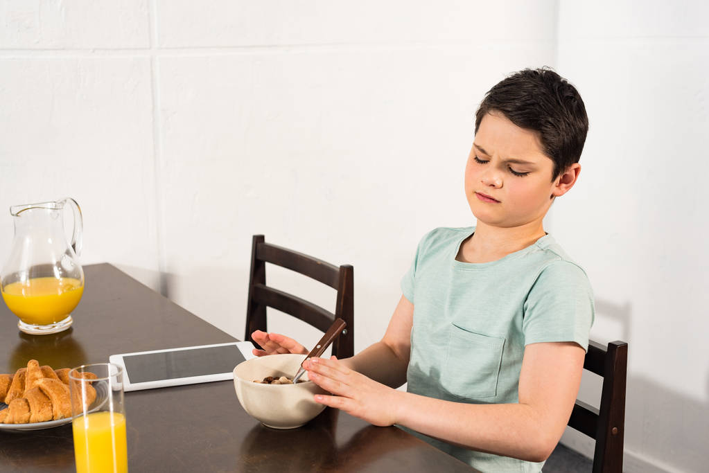 garçon insatisfait assis à la table et prendre le petit déjeuner dans la cuisine
 - Photo, image