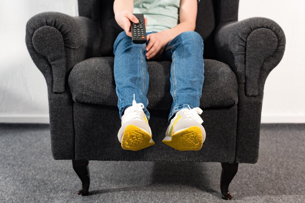 niño en jeans sentado en sillón y sosteniendo mando a distancia
 - Foto, imagen
