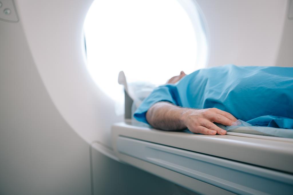 selectieve focus van patiënt liggend op CT-scanner bed tijdens tomografie test - Foto, afbeelding