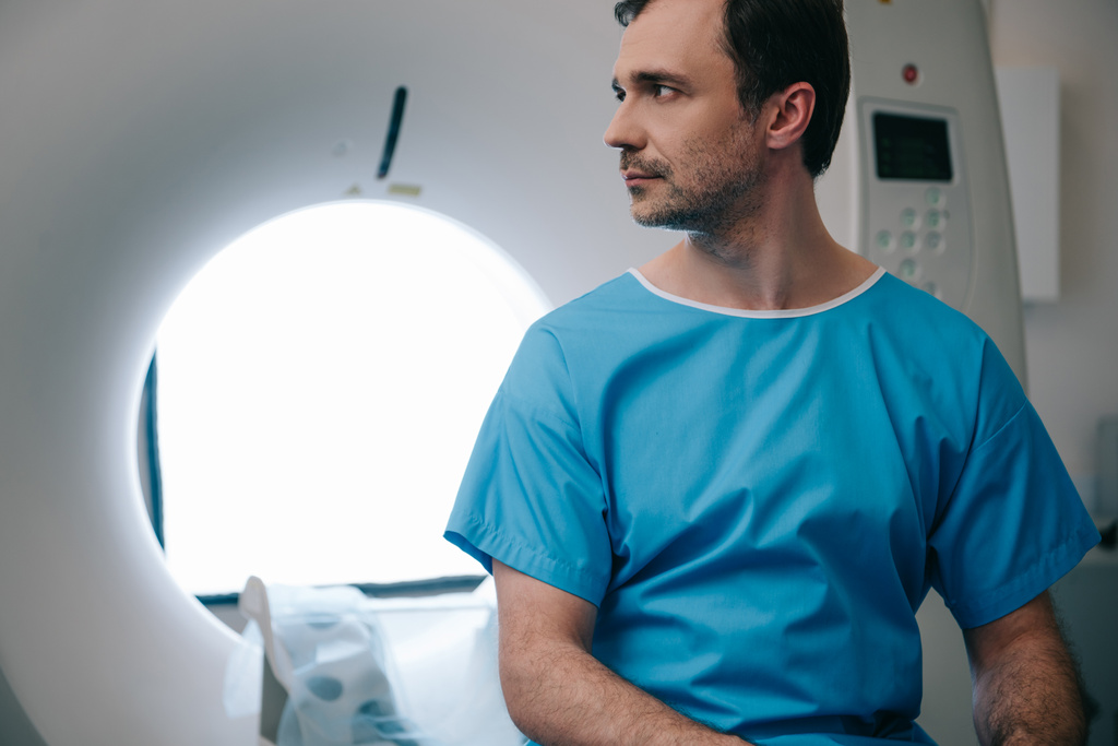 Nachdenklicher Patient sitzt im Krankenhaus auf Scanner-Bett und schaut weg - Foto, Bild