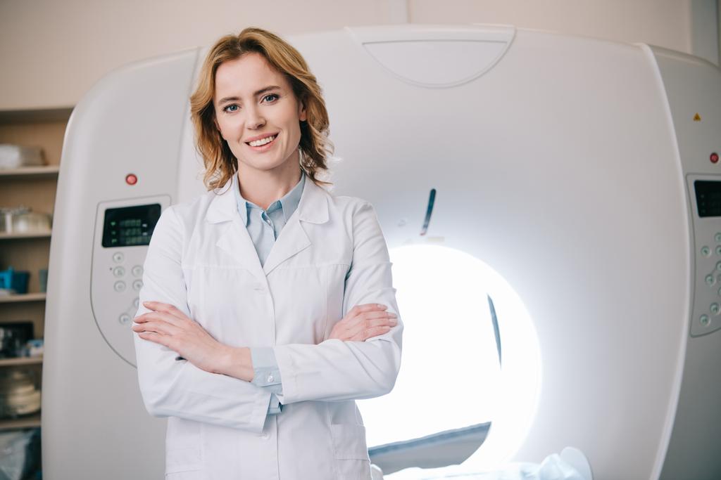 Veselý radiologista stojící u překřížené paže u vypočteného tomografie a pohled na kameru - Fotografie, Obrázek