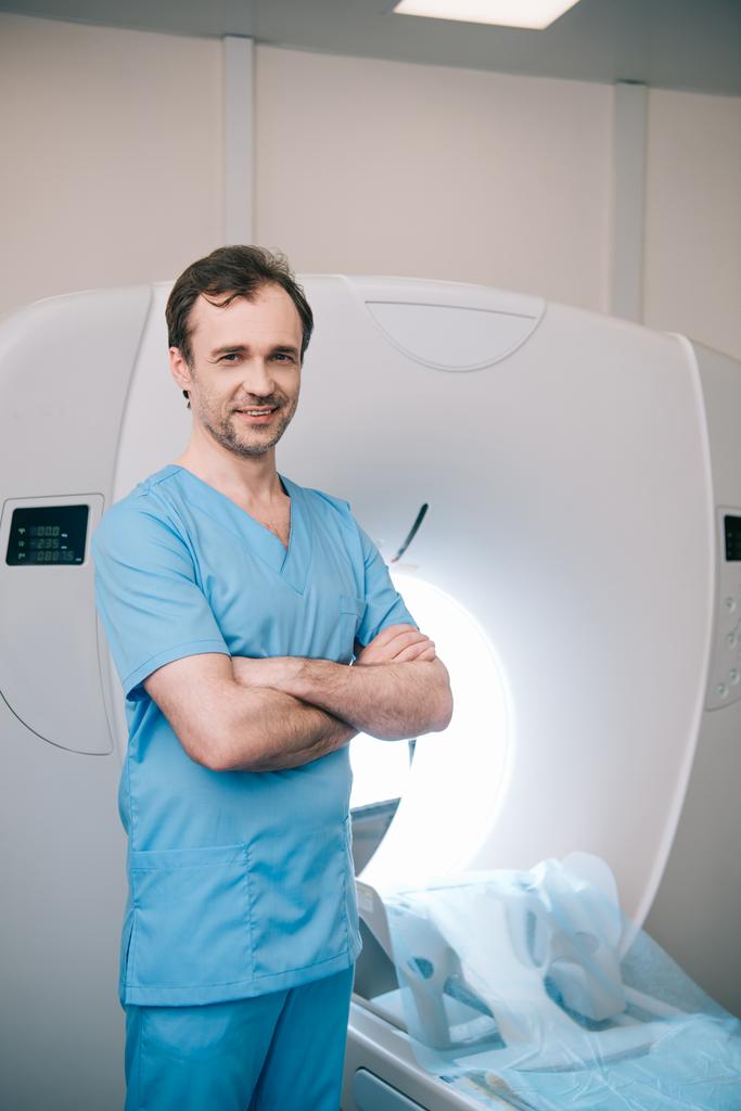 wesoły lekarz stojący obok skanera rezonansu magnetycznego z skrzyżowanymi ramionami i patrzący w kamerę - Zdjęcie, obraz