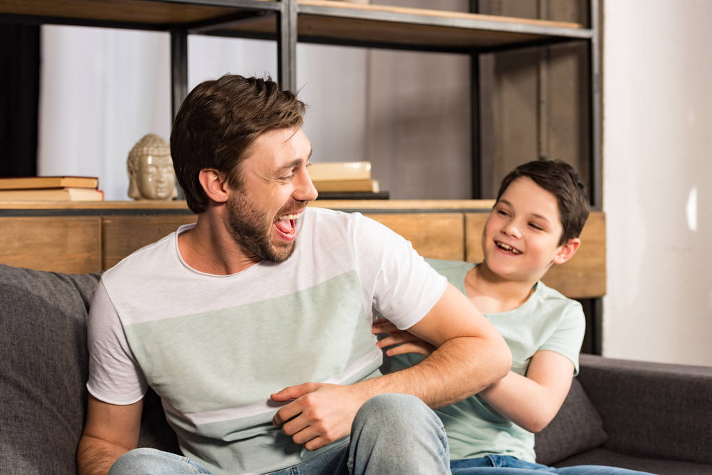 ridendo figlio e papà seduti sul divano e divertirsi in soggiorno
 - Foto, immagini