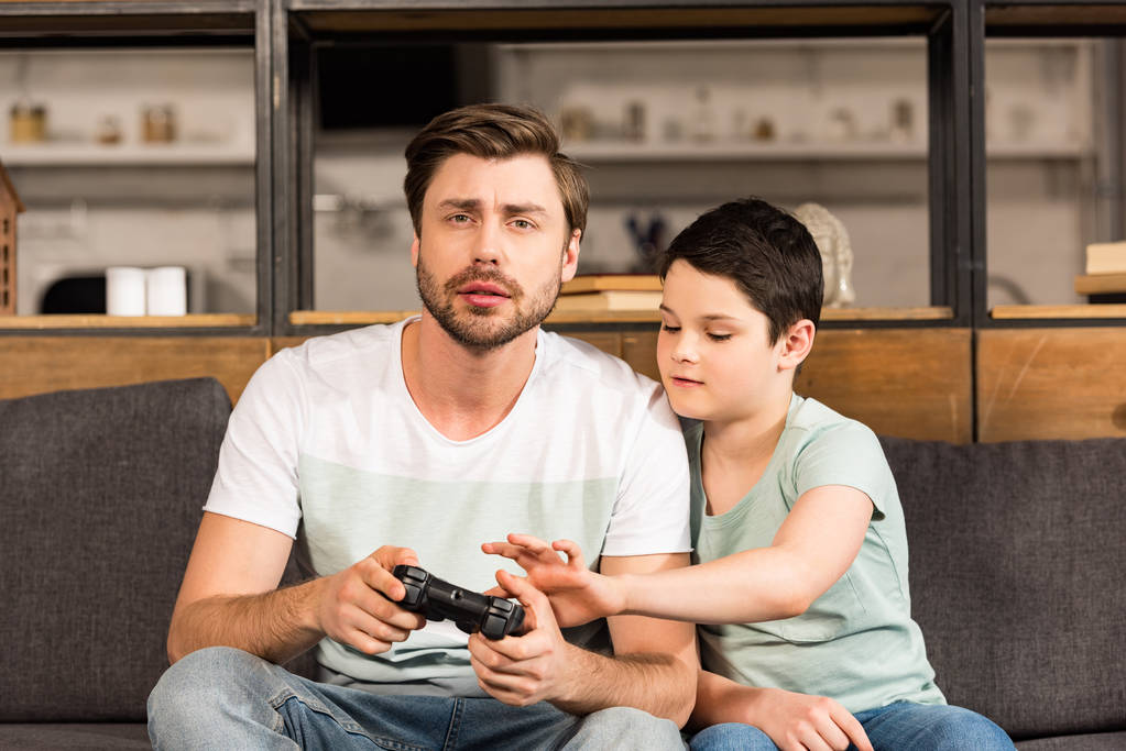 πατέρας και γιός κάθονται στον καναπέ και παίζοντας βιντεοπαιχνίδια - Φωτογραφία, εικόνα