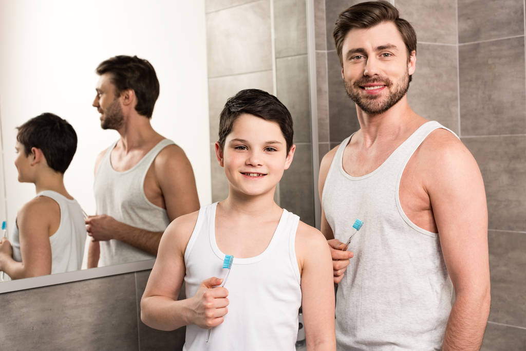 χαμογελαστός γιος και ο μπαμπάς βουρτσίζοντας τα δόντια το πρωί στο μπάνιο - Φωτογραφία, εικόνα