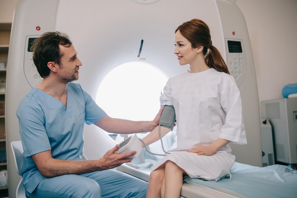 médico bonito medir a pressão arterial dos pacientes com tonômetro enquanto sentado no scanner de ressonância magnética
 - Foto, Imagem