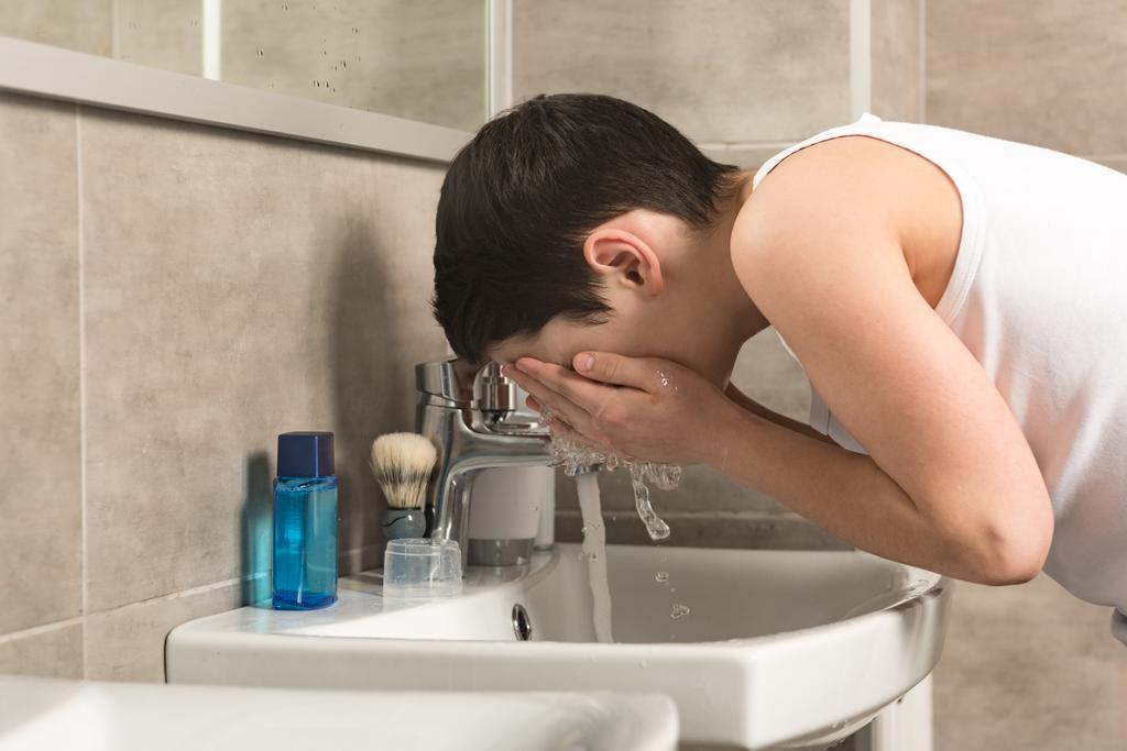 preteen fiú mosás arc reggel a fürdőszobában - Fotó, kép