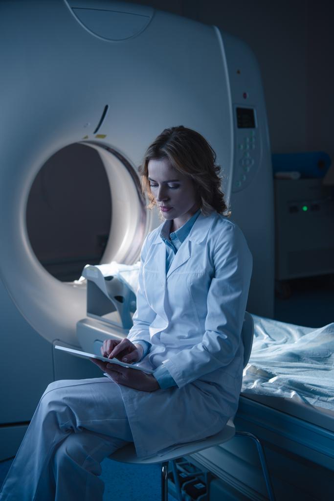 radiologiste réfléchi en utilisant une tablette numérique tout en étant assis près d'un scanner de tomodensitométrie
  - Photo, image