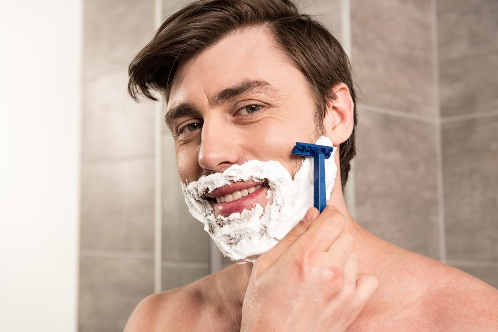 homme souriant rasage barbe avec rasoir dans la salle de bain
 - Photo, image