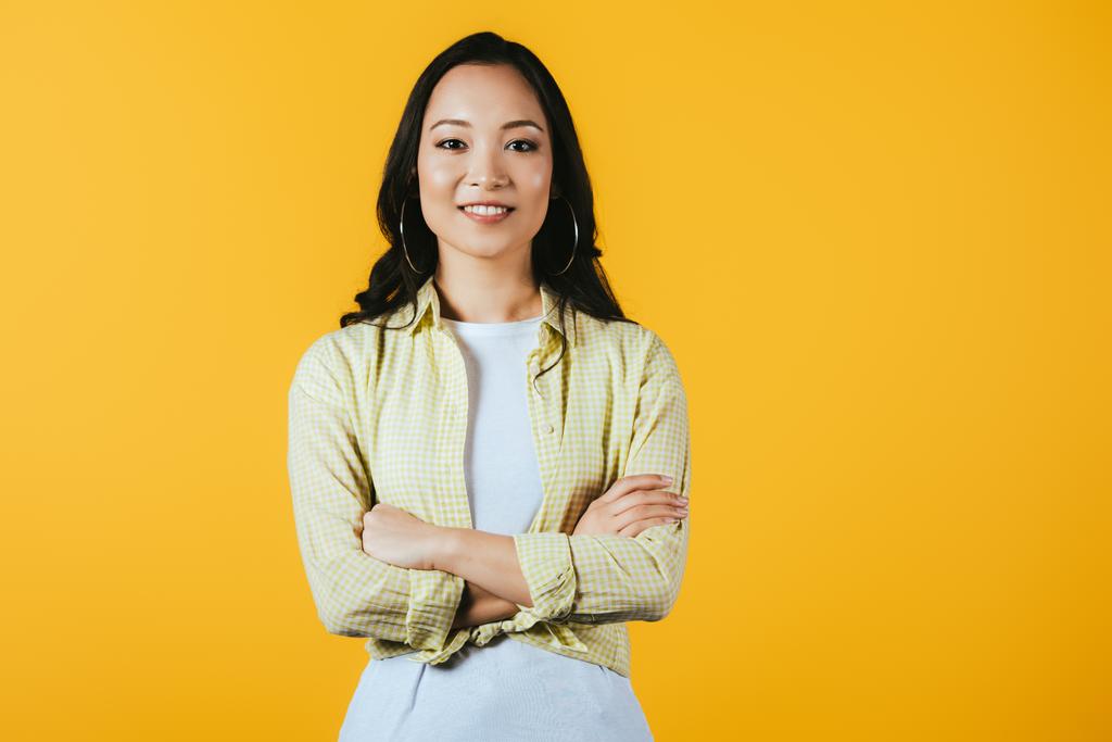 sonriente asiático chica con cruzado brazos aislado en amarillo
 - Foto, imagen