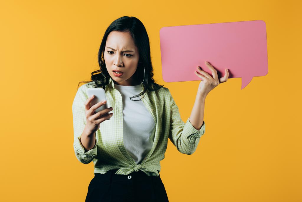 šokovaná Asijská dívka pomocí telefonu Smartphone a s růžovou řečí na žluté - Fotografie, Obrázek