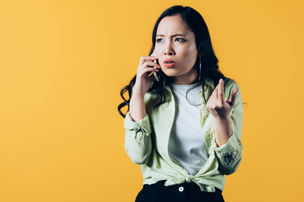aggódó ázsiai fiatal nő beszél okostelefon elszigetelt sárga  - Fotó, kép