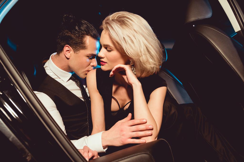 pohledný stylový muž objímající a líbání módní mladé ženy v autě - Fotografie, Obrázek