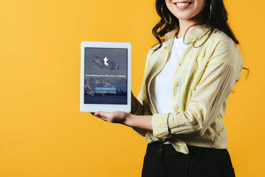 KYIV, UKRAINE - APRIL 16, 2019: cropped view of smiling girl showing digital tablet with tumblr app, isolated on yellow - Photo, Image