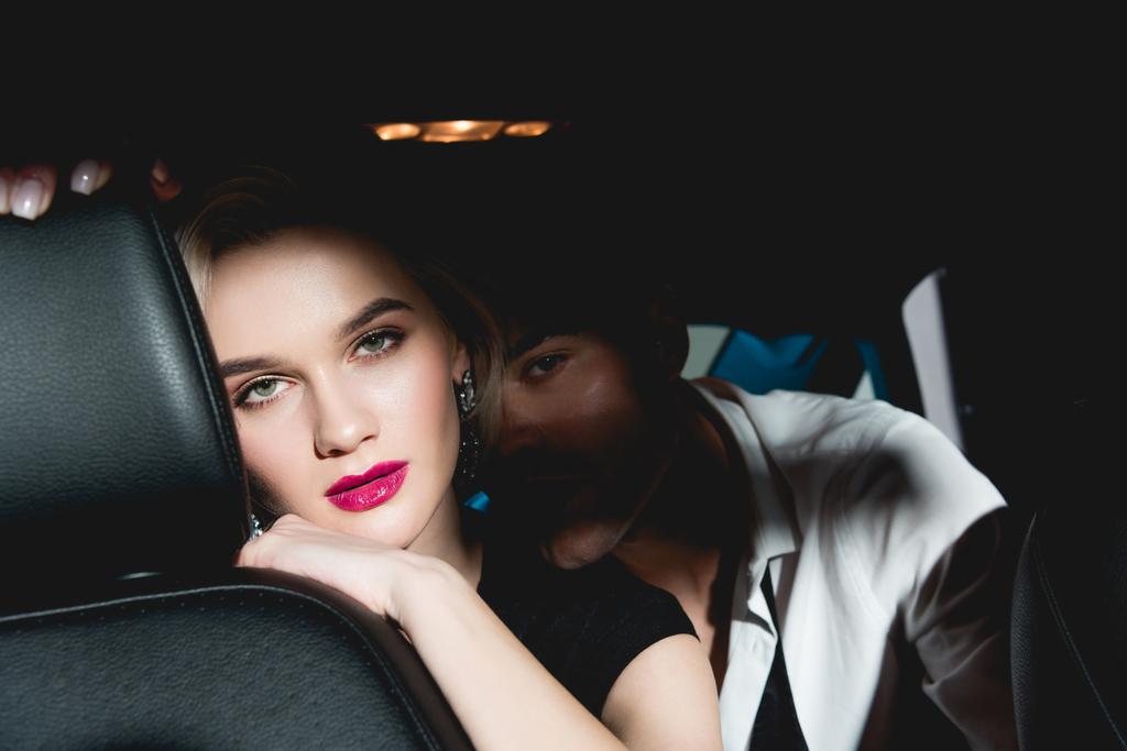 Mann und junge Frau sitzen im Dunkeln auf dem Rücksitz des Autos und schauen in die Kamera - Foto, Bild