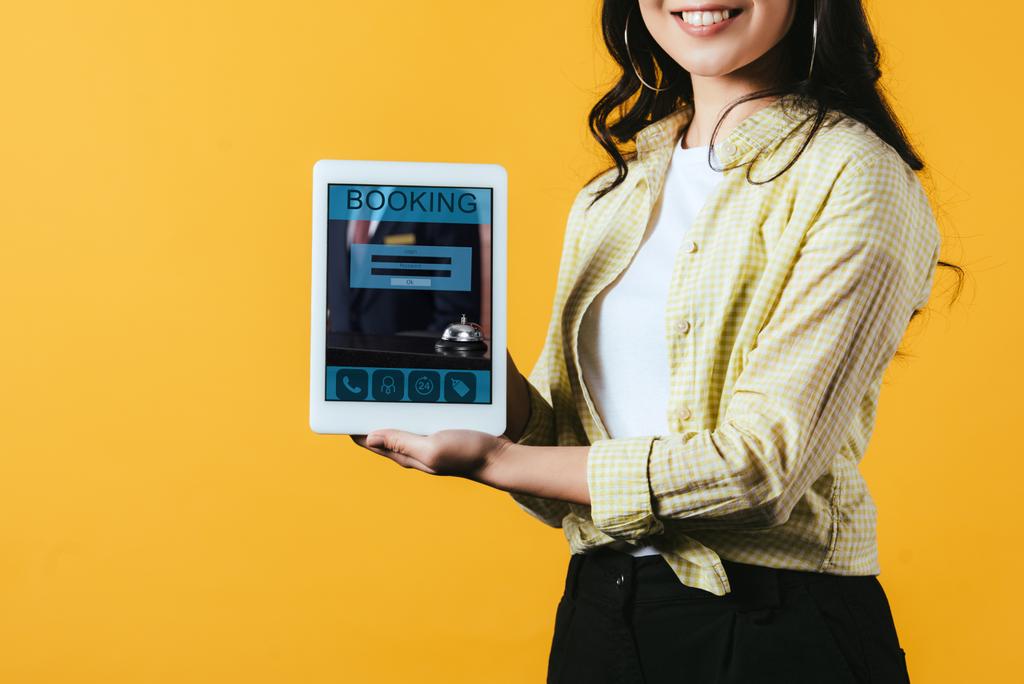 cropped view of girl showing digital tablet with booking app, isolated on yellow - Photo, Image