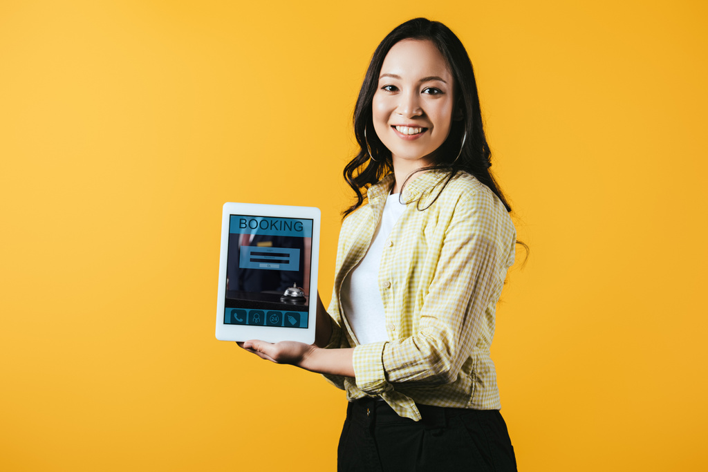 menina asiática mostrando tablet digital com aplicativo de reserva, isolado no amarelo
 - Foto, Imagem