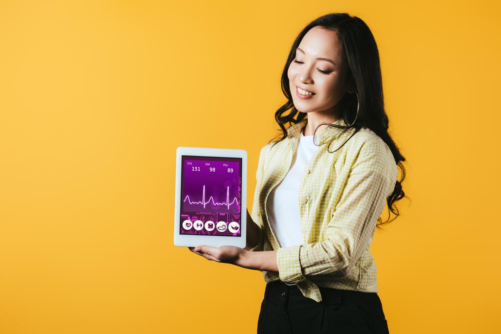 szczęśliwy Asian Dziewczyna pokazując cyfrowy tablet ze zdrowiem aplikacji, izolowane na żółtym - Zdjęcie, obraz