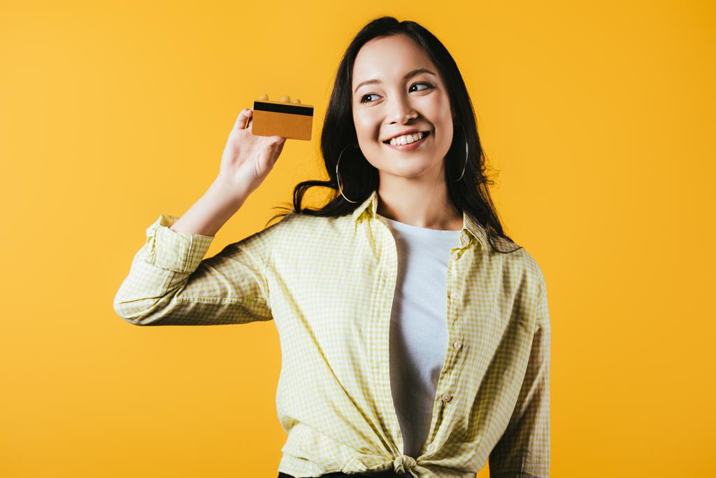 joyeuse asiatique fille tenant carte de crédit, isolé sur jaune
 - Photo, image