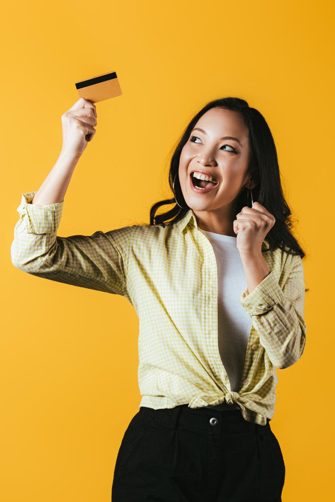 excité asiatique femme tenant carte de crédit, isolé sur jaune
 - Photo, image