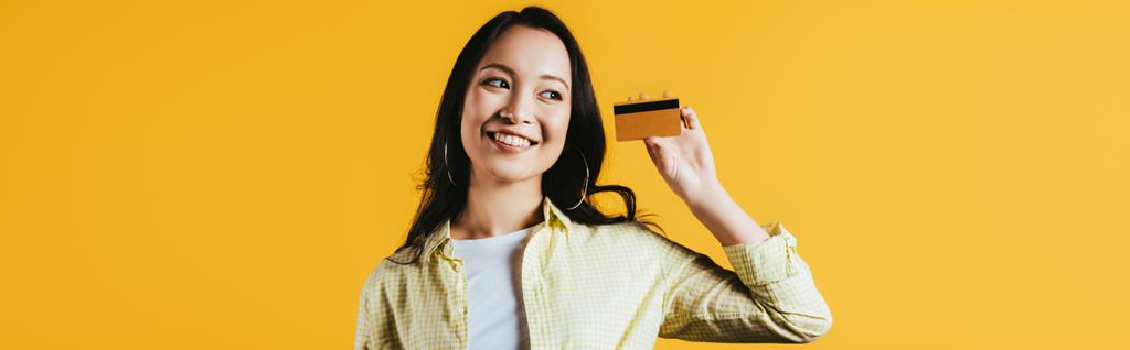 sorrindo asiático mulher segurando cartão de crédito, isolado no amarelo
 - Foto, Imagem