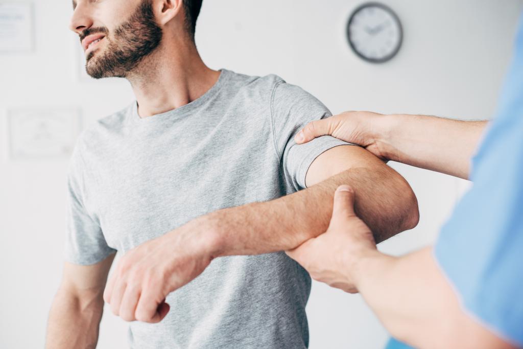 Kipusta kärsivän potilaan ja lääkärin valikoiva keskittyminen potilaan käsivarren tutkimiseen hierontakaapissa klinikalla
 - Valokuva, kuva