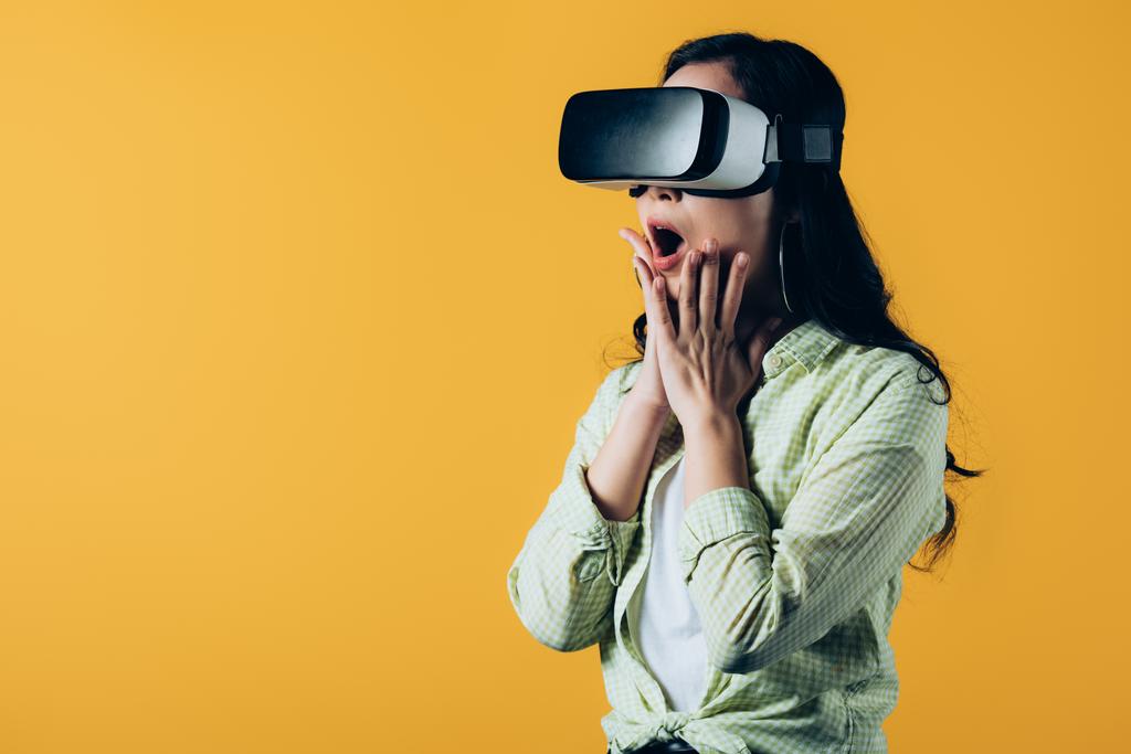 geschokt meisje dragen Virtual Reality headset, geïsoleerd op geel - Foto, afbeelding