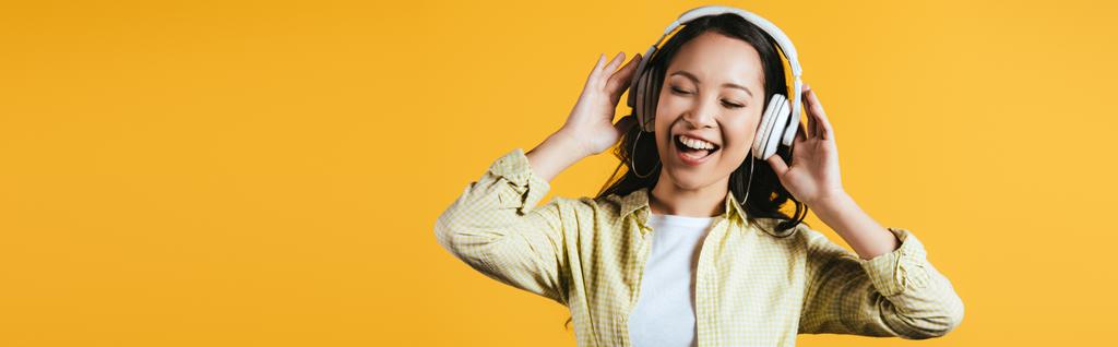 黄色で隔離されたヘッドフォンで音楽を歌い、聴く幸せなアジアの女の子 - 写真・画像
