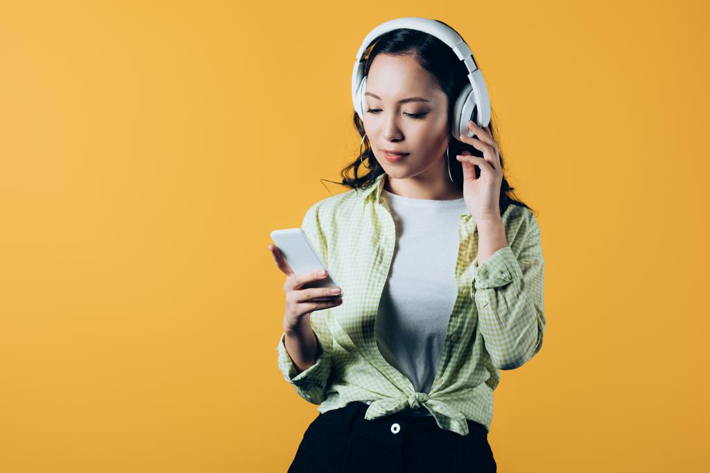 asian girl listening music with headphones and smartphone, isolated on yellow - Photo, Image
