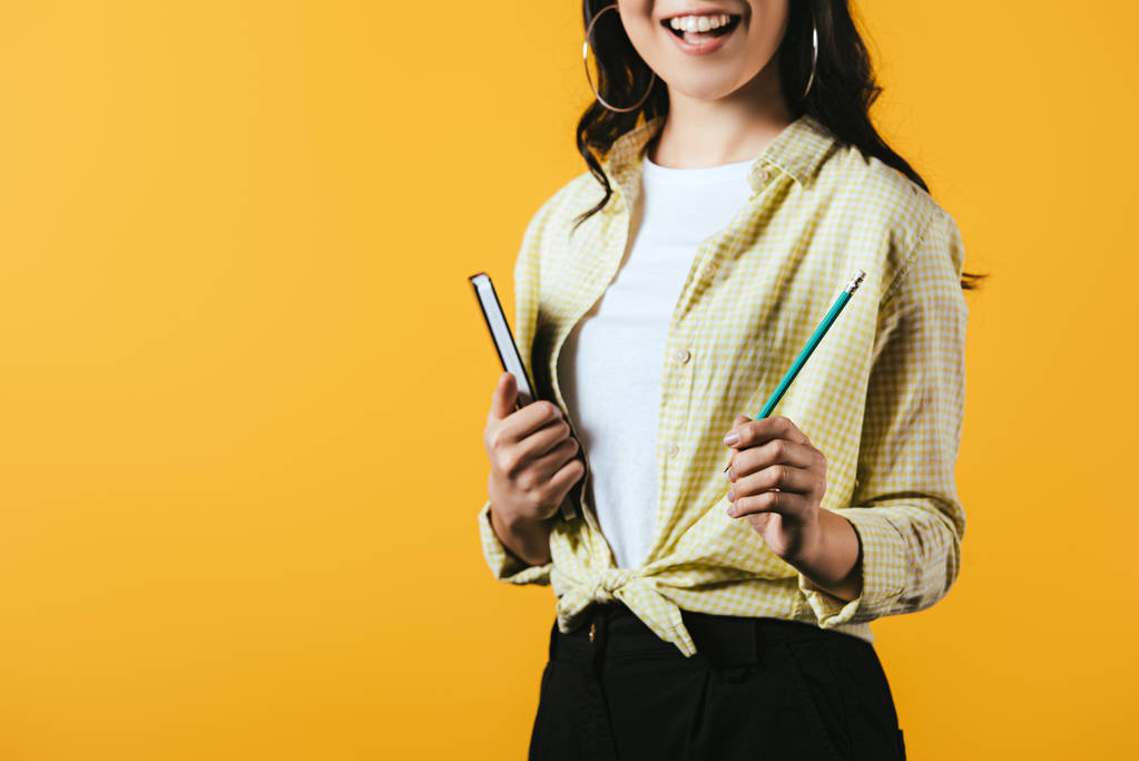 обрезанный вид улыбающейся девушки с ноутбуком и ручкой, изолированный на желтый
  - Фото, изображение