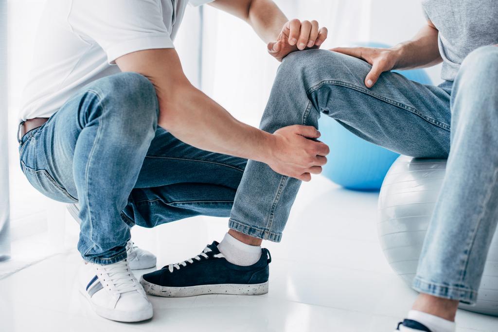 visão recortada do fisioterapeuta massagem perna do paciente sentado na bola de fitness no hospital
 - Foto, Imagem