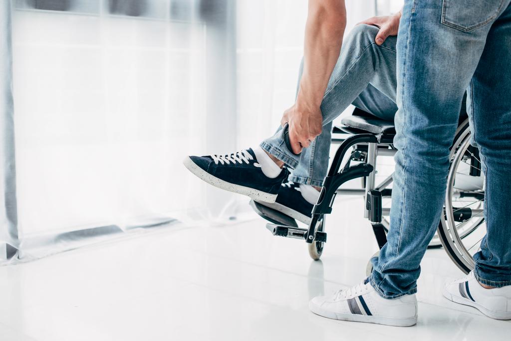 Vista recortada del fisioterapeuta masajeando pierna del paciente en silla de ruedas en el hospital
 - Foto, imagen