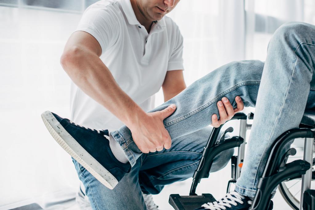 recortado vista de fisioterapeuta masaje pierna de discapacitado hombre en silla de ruedas
  - Foto, Imagen