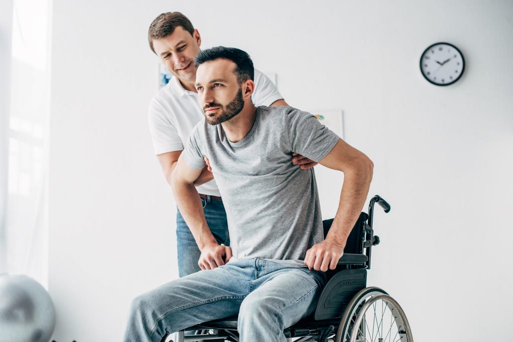 Fysiotherapeut helpen gehandicapten man in een rolstoel tijdens het herstel in het ziekenhuis - Foto, afbeelding